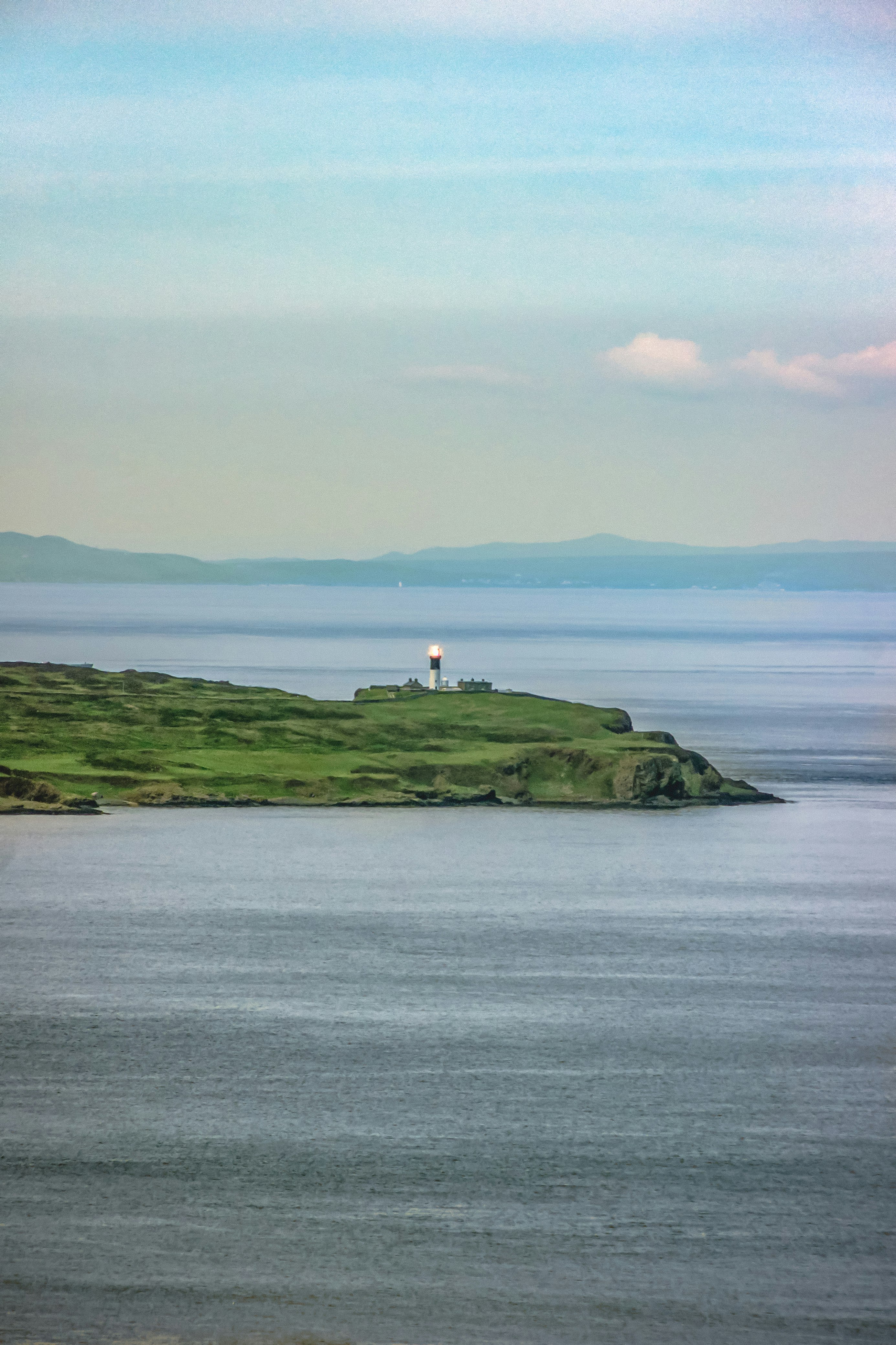 white lighthouse on green grass covered hill by the sea under white clouds during daytime